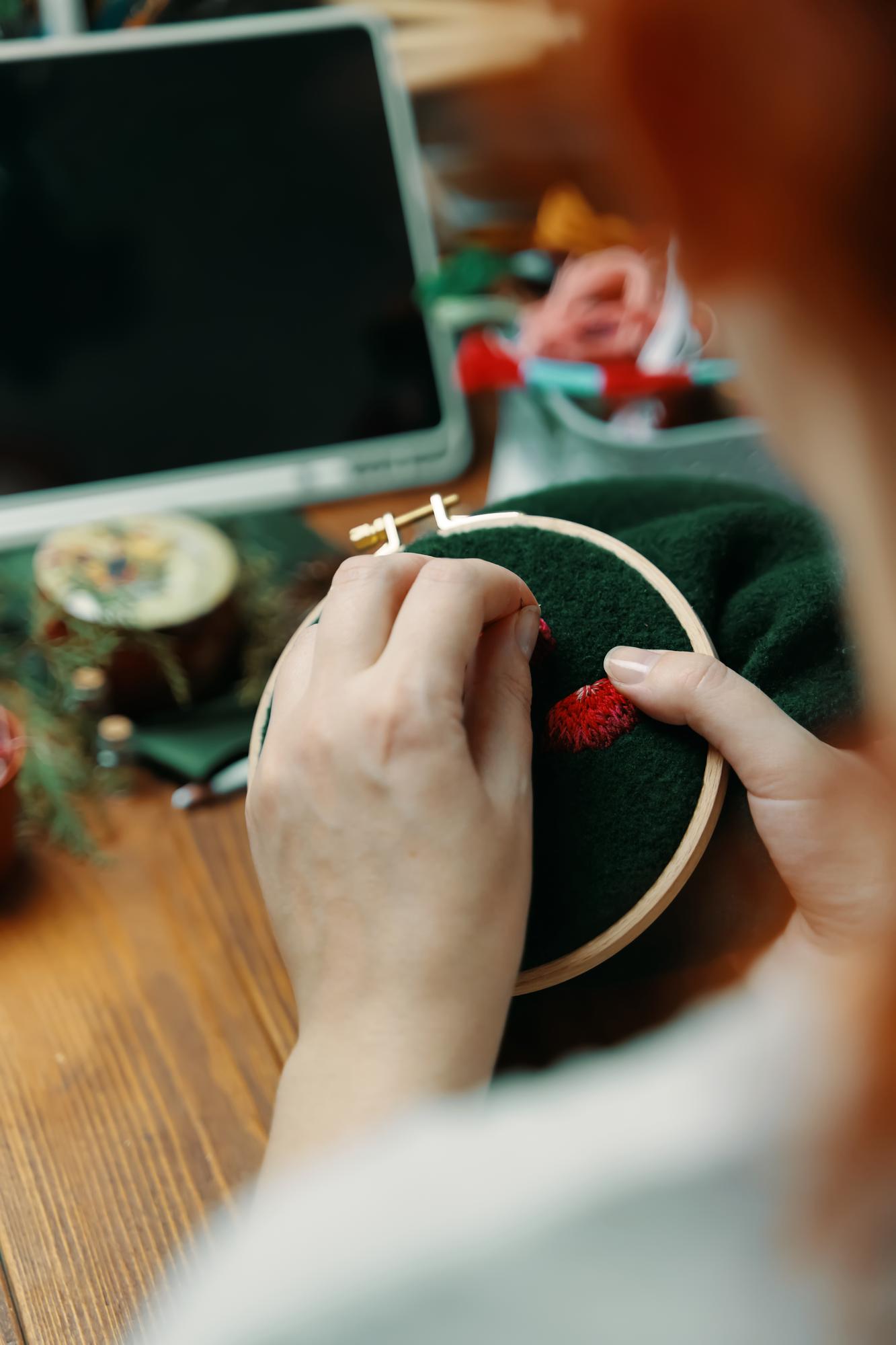Mani che preparano tessuto per ricamo su tavolo minimal